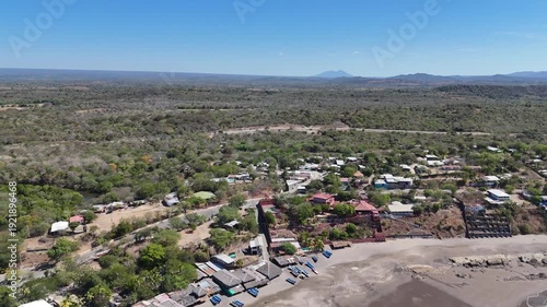 An aerial view of a small town surrounded by green trees and mountains on a sunny day. The town has many houses and roads.