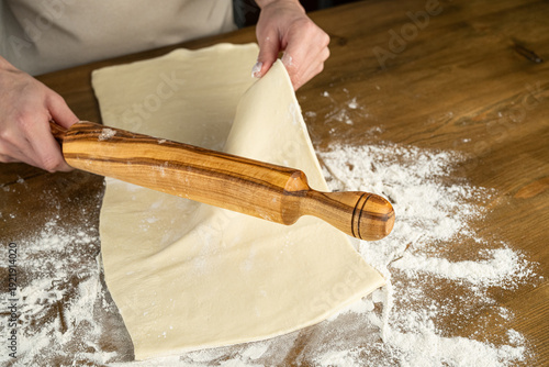 Person Rolling Dough on Wooden Table in Kitchen