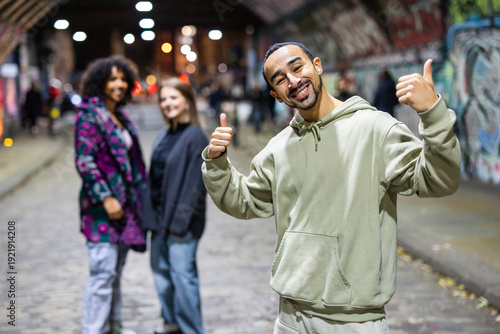 Man giving thumbs up with friends walking in urban tunnel
