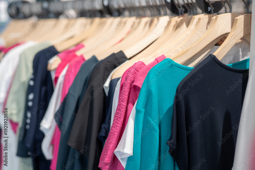 Obraz premium Clothes hanging on wooden hangers in a store displaying different colors and styles during the day for shoppers to see and choose