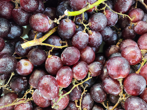 Close-up of fresh red grapes with water droplets at a local market. These organic seedless grapes are harvested for their sweet taste, providing a healthy, juicy, and antioxidant-rich snack.