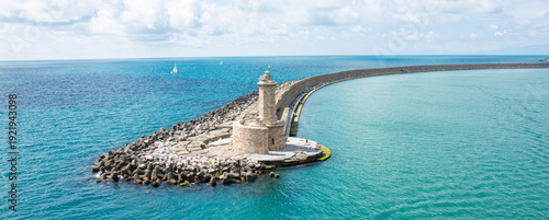 Historic lighthouse on stone pier surrounded by turquoise sea coastal landmark