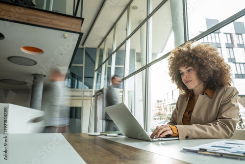 Fotografie Businesswoman typing on laptop in busy modern office