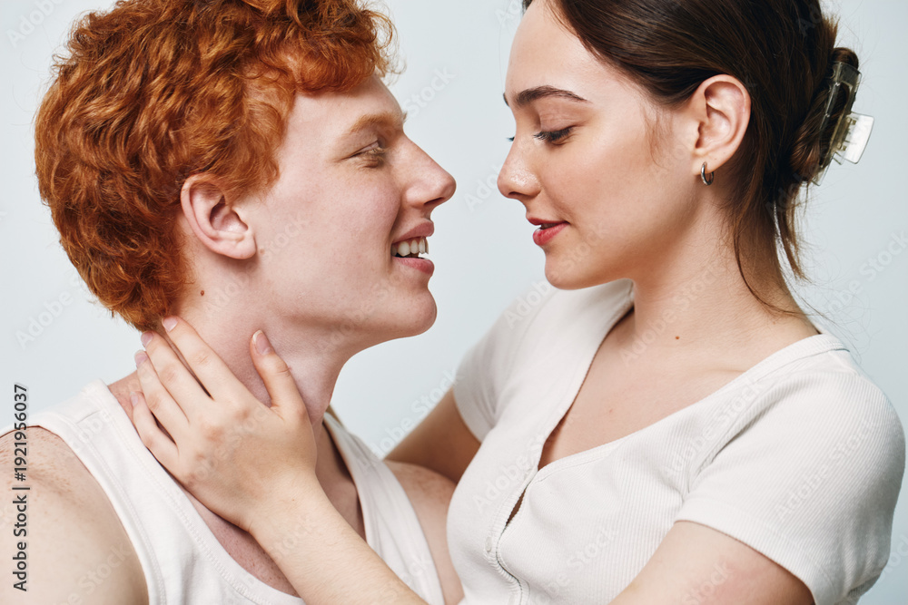 Naklejka premium Couple in intimate moment with woman holding man neck, closeup of young woman and man looking at each other with affection on neutral background.