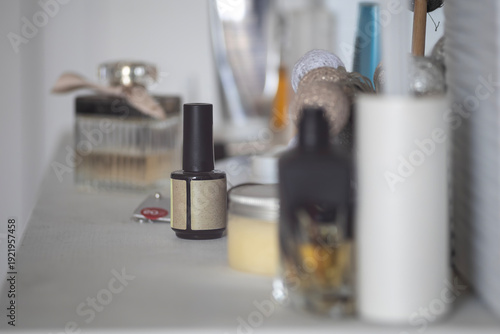 Selection of cosmetic bottles including perfume and nail polish standing on a white shelf. Shallow depth of field highlights the glass containers and home beauty products in a bright room area.