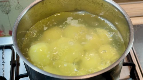Boiling peeled potatoes in pot on gas stove, golden chunks simmering in bubbling water, gentle steam rising, home cook prepping.