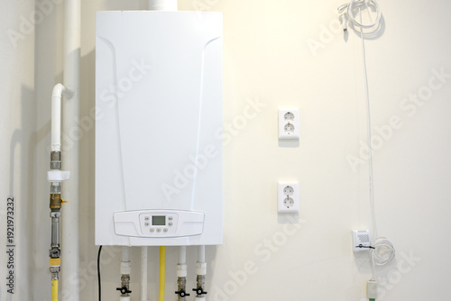 White tankless water heater mounted on wall with pipes and outlets visible