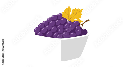 A white square-shaped bowl is abundantly overflowing with dark purple grapes and features a single withered yellow leaf on a white background.