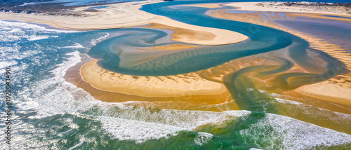 Breathtaking Aerial View of a Winding River Delta Meeting the Turquoise Ocean with Golden Sandbanks, Intricate Water Channels, and Crashing White Surf in a Pristine Coastal Landscape Environment.