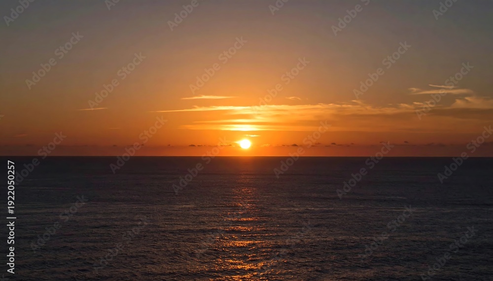 Obraz premium A vibrant sunset over the ocean. The sun is a bright orange orb reflected on the water's surface, with soft clouds