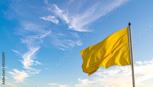 A vibrant yellow flag flutters gracefully on a pole, set against a backdrop of a bright blue sky with wispy clouds