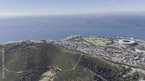 Drone lowers from view of Robben Island and Green Point, down behind Signal Hill on a sunny morning in Cape Town, South Africa