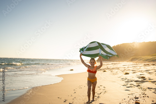 A girl running with a towel at the beach pretending to have a cap.