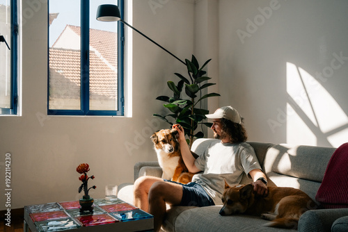 Man relaxes on couch with two dogs in sunny living room