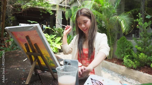 Gen Z Influencer content creator woman using smartphone with creativity leisure painting brush on canvas at workshop cafe
