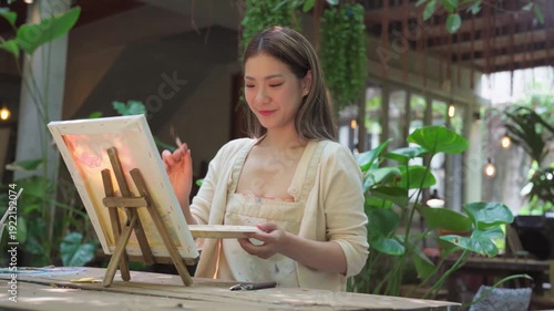 Authentic Gen Z happy young adult asian woman painting brush on canvas at workshop cafe creativity lifestyle therapy