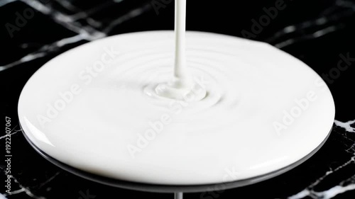 A stream of white liquid falling onto a round surface creating ripples