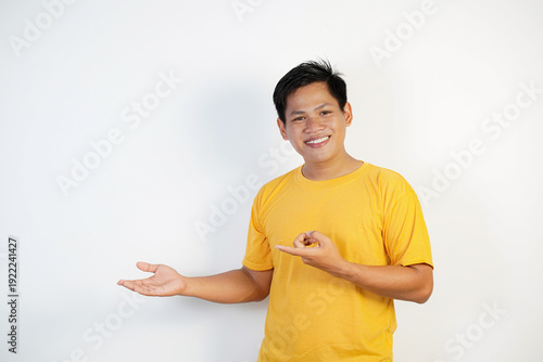 Young Asian man in a yellow shirt smiling cheerfully, feeling happy and pointing to the side, showing object in copy space	