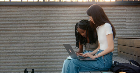 Two young students working on laptop outdoors in university campus