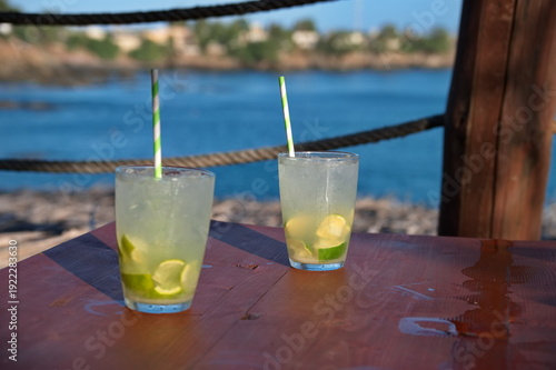Two glasses with cocktail on the wooden table in restaurant above the beach