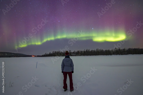 Stunning Aurora Borealis dancing over frozen Lake Inari and snowy forest in Ivalo, Finnish Lapland