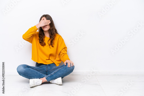 Schilderij op canvas Young caucasian woman sitting on the floor isolated on white wall covering eyes by hands