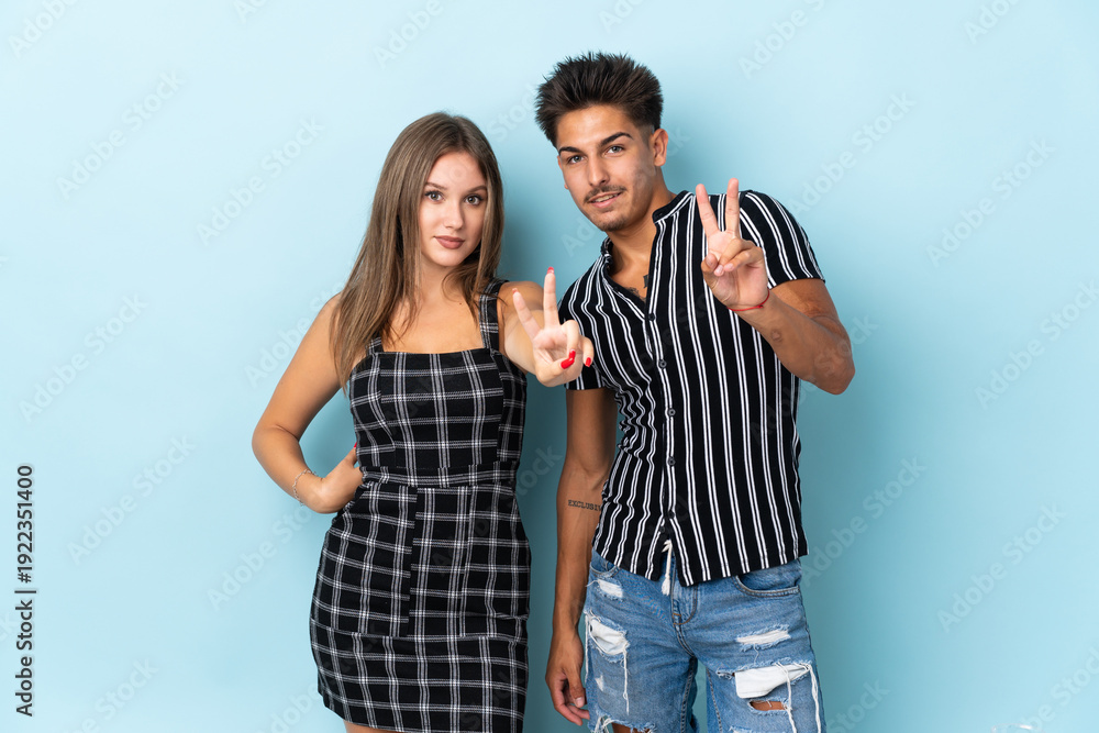 Naklejka premium Teenager caucasian couple isolated on blue background smiling and showing victory sign