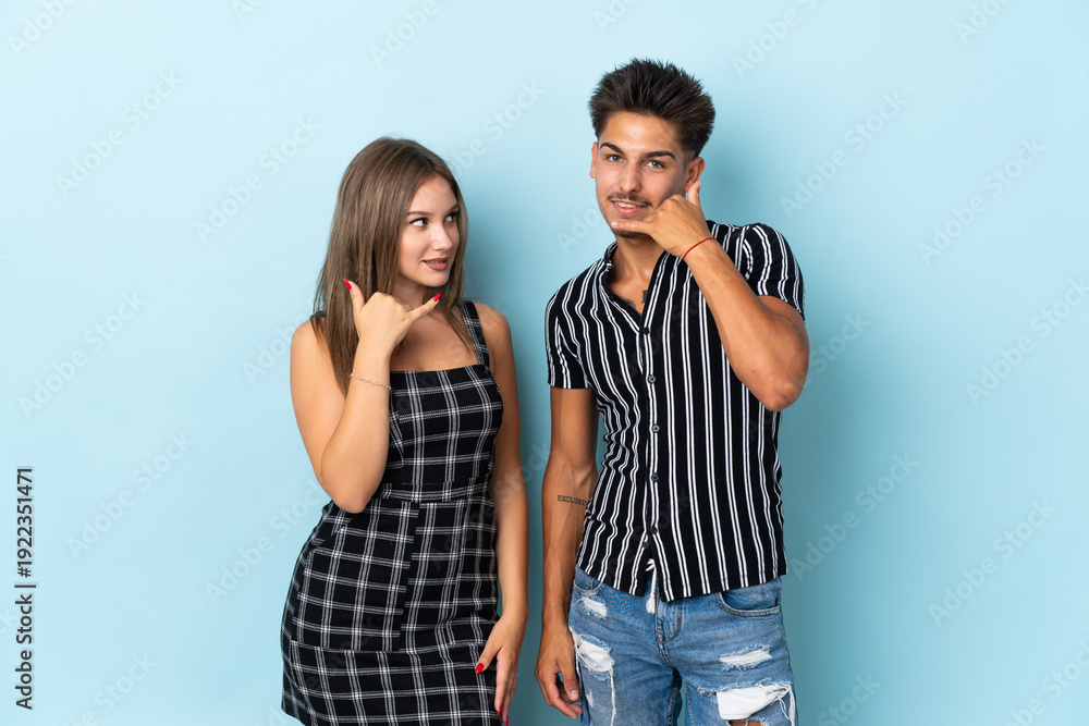 Naklejka premium Teenager caucasian couple isolated on blue background making phone gesture. Call me back sign