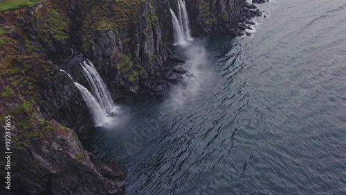 Waterfalls cascading down rocky cliffs into a calm sea, showcasing the natural beauty of the landscape with lush greenery and textured rock formations in the background