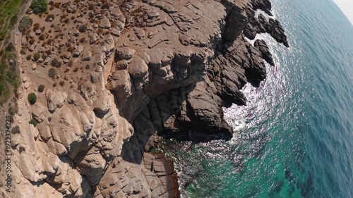 Rocky coastal cliffs with turquoise water and sunlight reflections, showcasing the gradual transition of land to sea in a serene natural landscape
