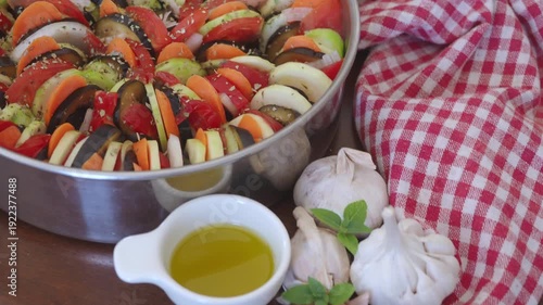 Garlic bulbs and olive oil near Ratatouille. red checkered napkin. Delicious Mediterranean meal, inspired French Italian cuisine. Traditional vegetable ratatouille. Seasonal autumn dish. Vegan tian 4K