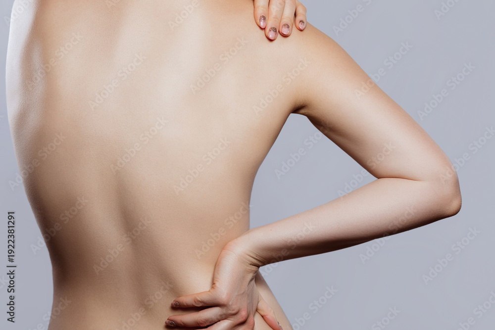 Fototapeta premium Women experiencing back pain while holding her back in a studio setting