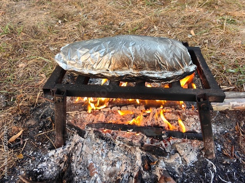 Cooking food in foil over a fire, grilling fish outdoors.