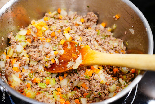 Bolognese base with mince cooking in a silver pan with a wooden spoon