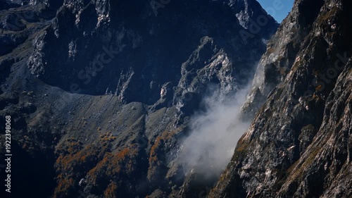 Aerial view of Montenegro high mountains Prokletije, scree slopes, and a narrow alpine valley as the camera pans, fog drifts, and autumn foliage clings