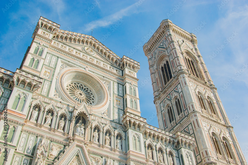 Fototapeta premium The intricate marble facade and Giotto's Campanile of the Florence Cathedral against a blue sky.