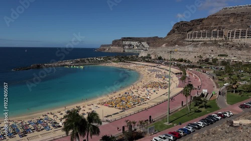 Sunny crowded volcanic beach with turquoise sea panorama