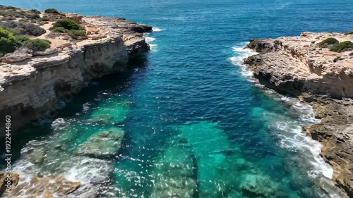 Coastal rocky inlet with clear turquoise water and visible stone formations, showcasing the natural beauty of the shoreline and surrounding vegetation under bright sunlight