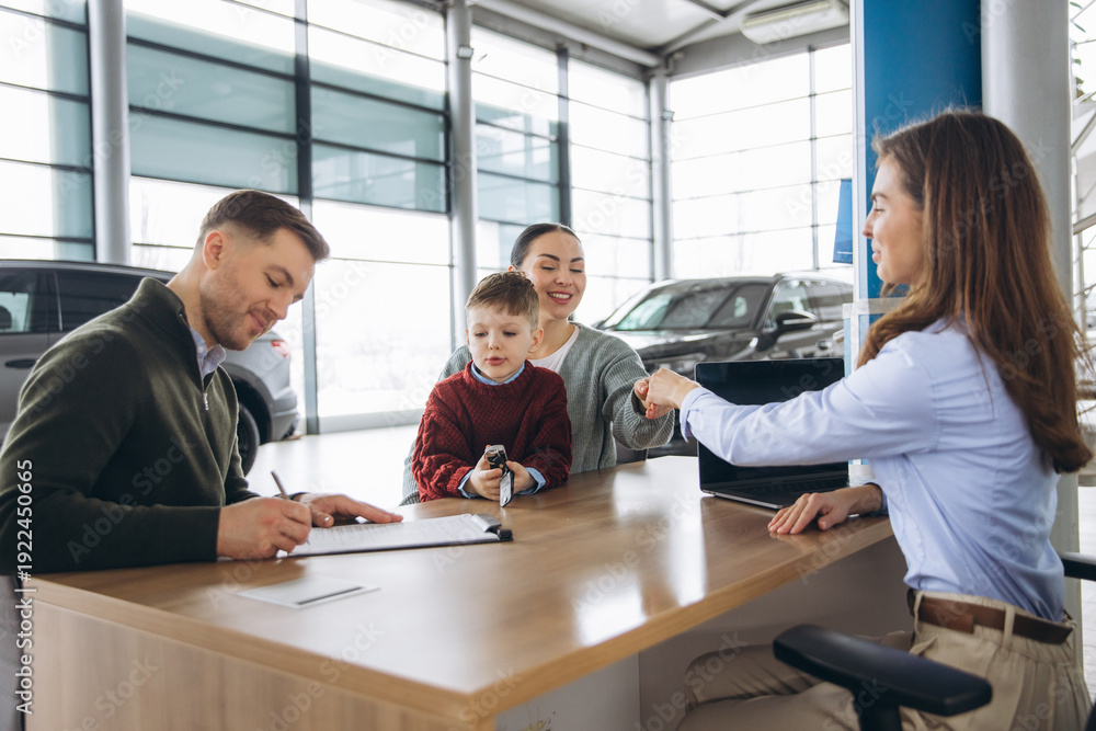 Fototapeta premium Family buying new car at dealership signing contract, receiving key from saleswoman, happy parents and child