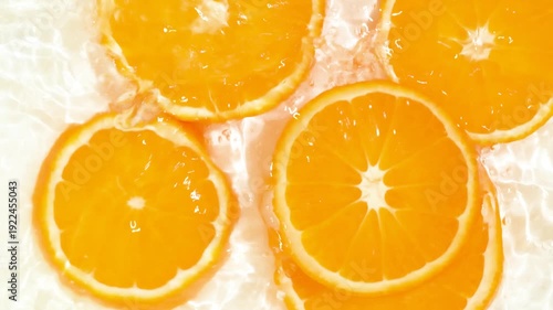 Cinematic splash of water as orange slices fall from above, top view.
