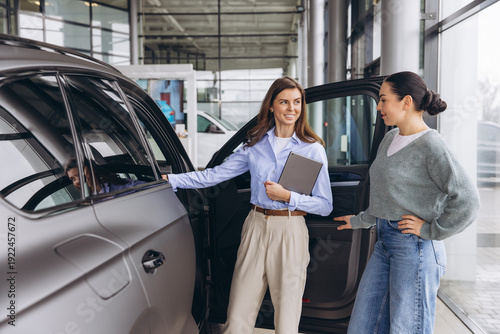 Slika na platnu Saleswoman showing new car to female customer in modern auto dealership, experie