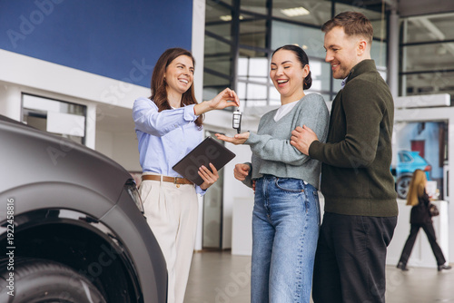 Valokuva Salesperson handing over car keys to happy young couple purchasing new vehicle a