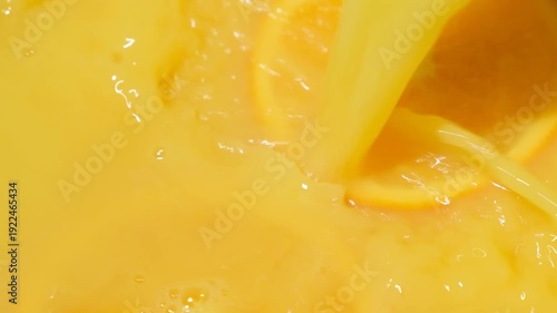 Macro shot of orange juice stream pouring on ripe citrus circles.