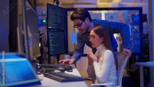 Asian programmers collaborating on software development at night, focused on writing code across multiple monitors in a tech office environment Programmers Collaborating on Software Development	