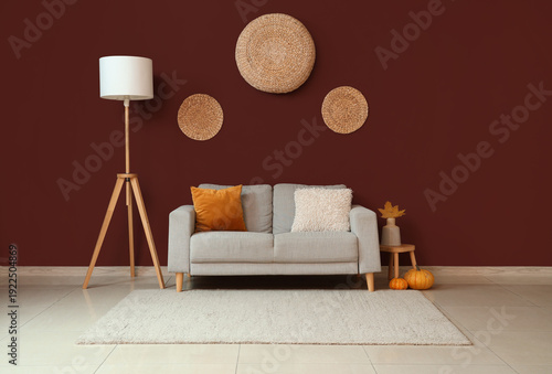 Φωτογραφία Comfortable sofa, floor lamp and autumn decor near red wall in interior of livin