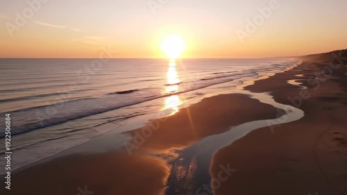 Sunrise over tranquil beach with gentle waves lapping at sandy shore, reflecting golden light and creating a serene coastal landscape at dawn