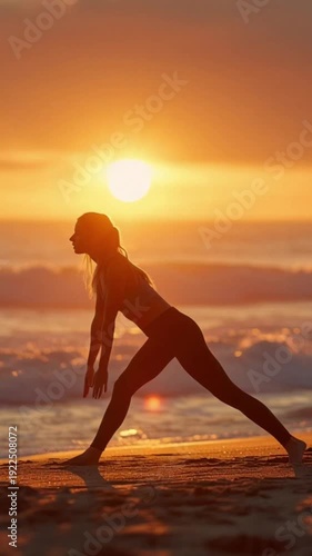 Silhouette of a young woman practicing yoga warrior pose on a sandy beach at a stunning golden sunset with dramatic clouds and glowing orange sky, wellness and mindfulness concept

