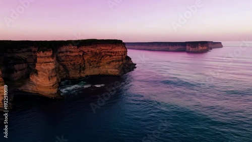 Coastal cliffs at sunset with calm ocean waves reflecting warm colors, showcasing the gradual transition of light and landscape in a serene natural setting