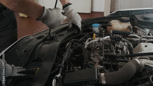 Medium shot of hands of two unrecognizable male car mechanic colleagues examining engine while servicing automobile in garage, pointing at spark plugs and cylinders to find reason for engine misfire
