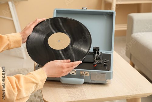 Tableau sur toile Young woman putting vinyl disk into retro record player in living room, closeup
